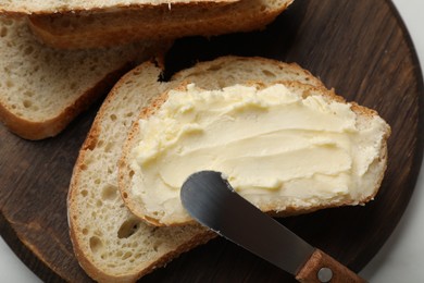 Photo of Fresh bread with butter and knife on white table, top view