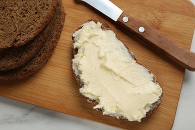 Photo of Fresh bread with butter and knife on white table, top view