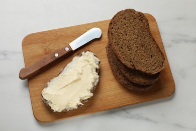 Photo of Fresh bread with butter and knife on white marble table, top view