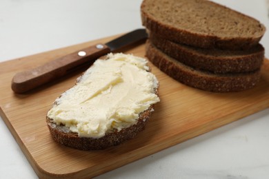 Photo of Fresh bread with butter and knife on white table, closeup