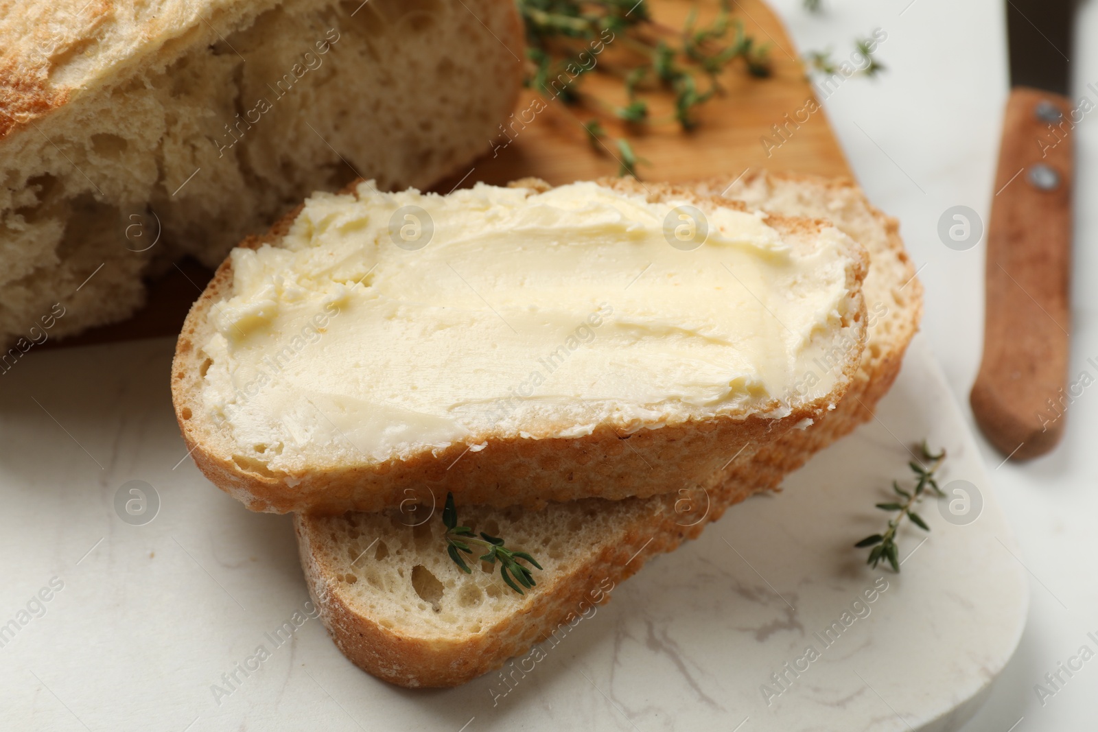 Photo of Fresh bread with butter and thyme on white table, closeup