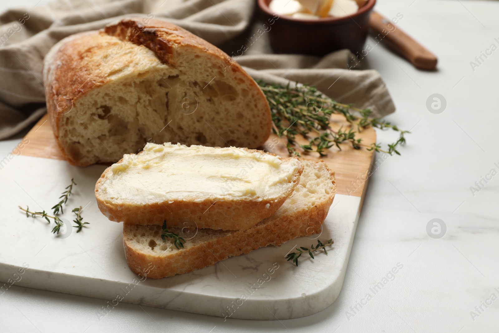 Photo of Fresh bread with butter and thyme on white table, closeup