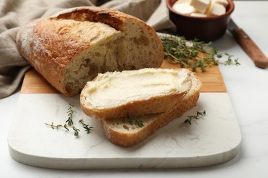 Photo of Fresh bread with butter and thyme on white table, closeup