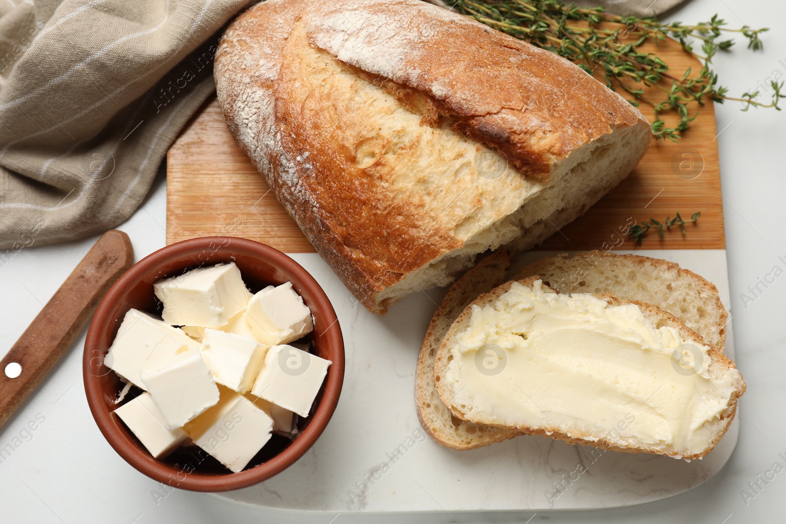 Photo of Fresh bread with butter and thyme on white table, flat lay