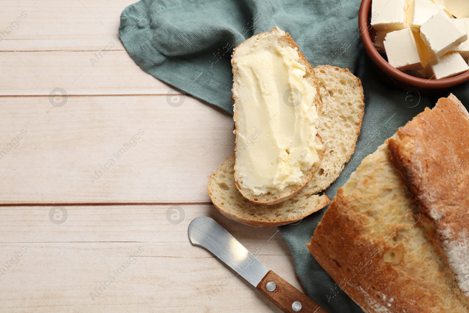 Photo of Fresh bread with butter and knife on light wooden table, flat lay. Space for text