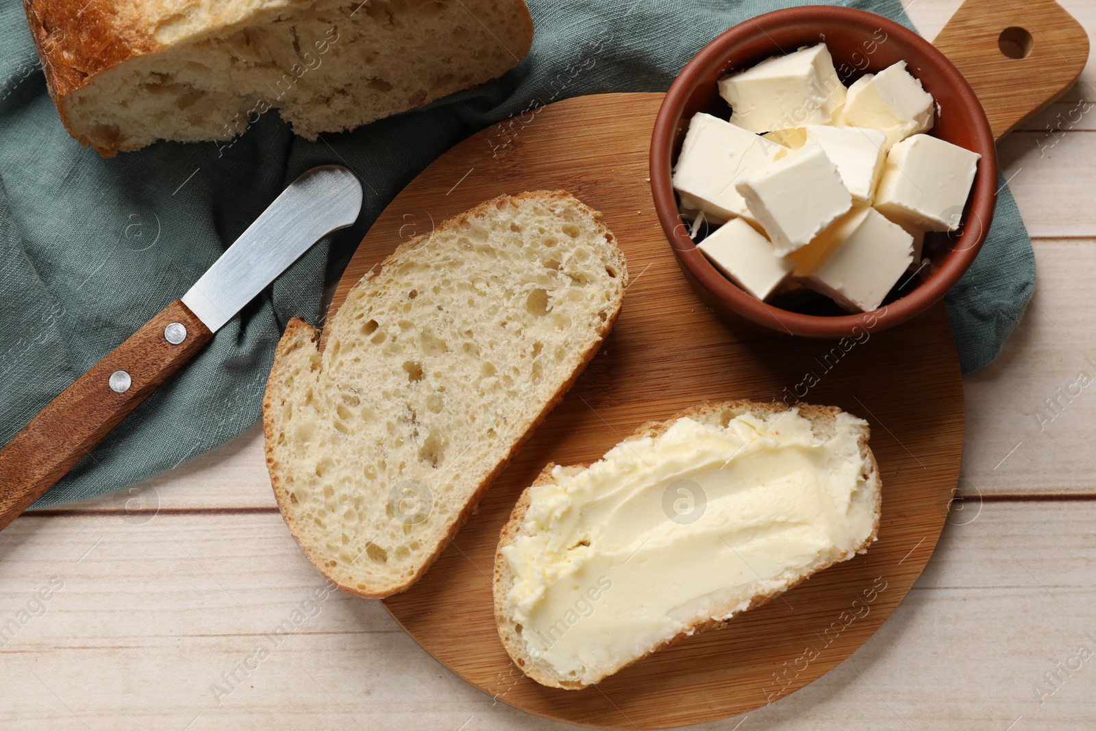 Photo of Fresh bread with butter and knife on light wooden table, flat lay