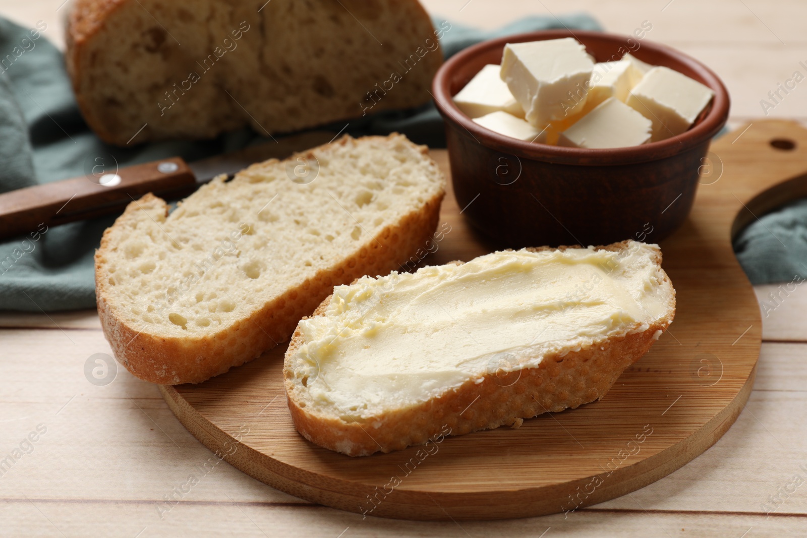 Photo of Fresh bread with butter on light wooden table, closeup