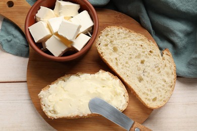 Photo of Fresh bread with butter and knife on light wooden table, top view