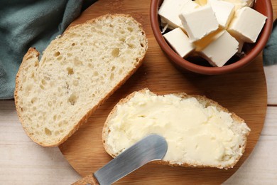 Fresh bread with butter and knife on light wooden table, top view