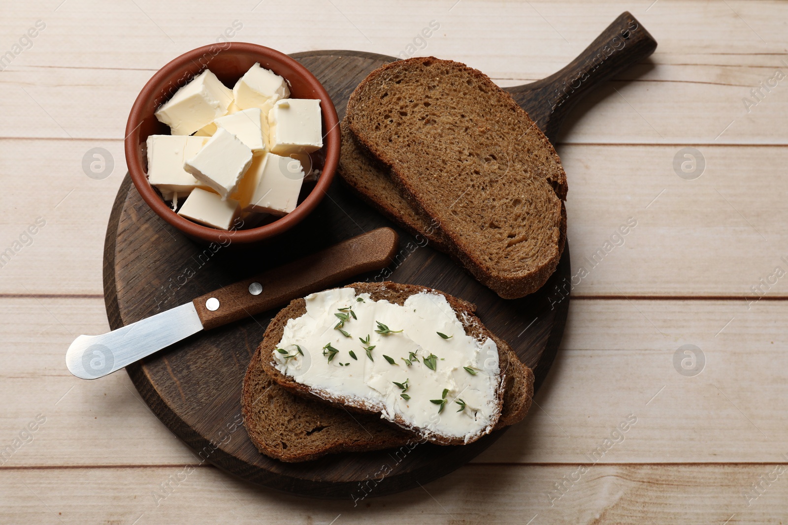 Fresh bread with butter, thyme and knife on light wooden table, top view Photo of Fresh bread with butter, thyme and knife on light wooden table, top view