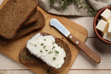 Photo of Fresh bread with butter, thyme and knife on light wooden table, flat lay