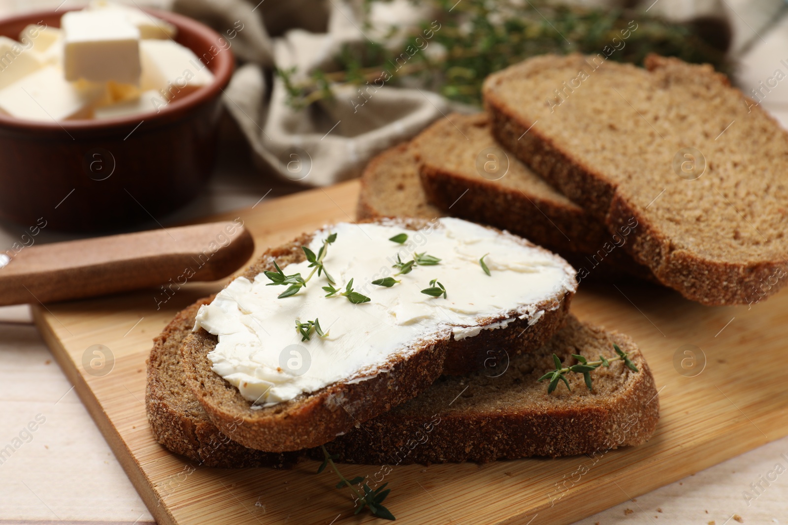 Photo of Fresh bread with butter, thyme and knife on light table, closeup