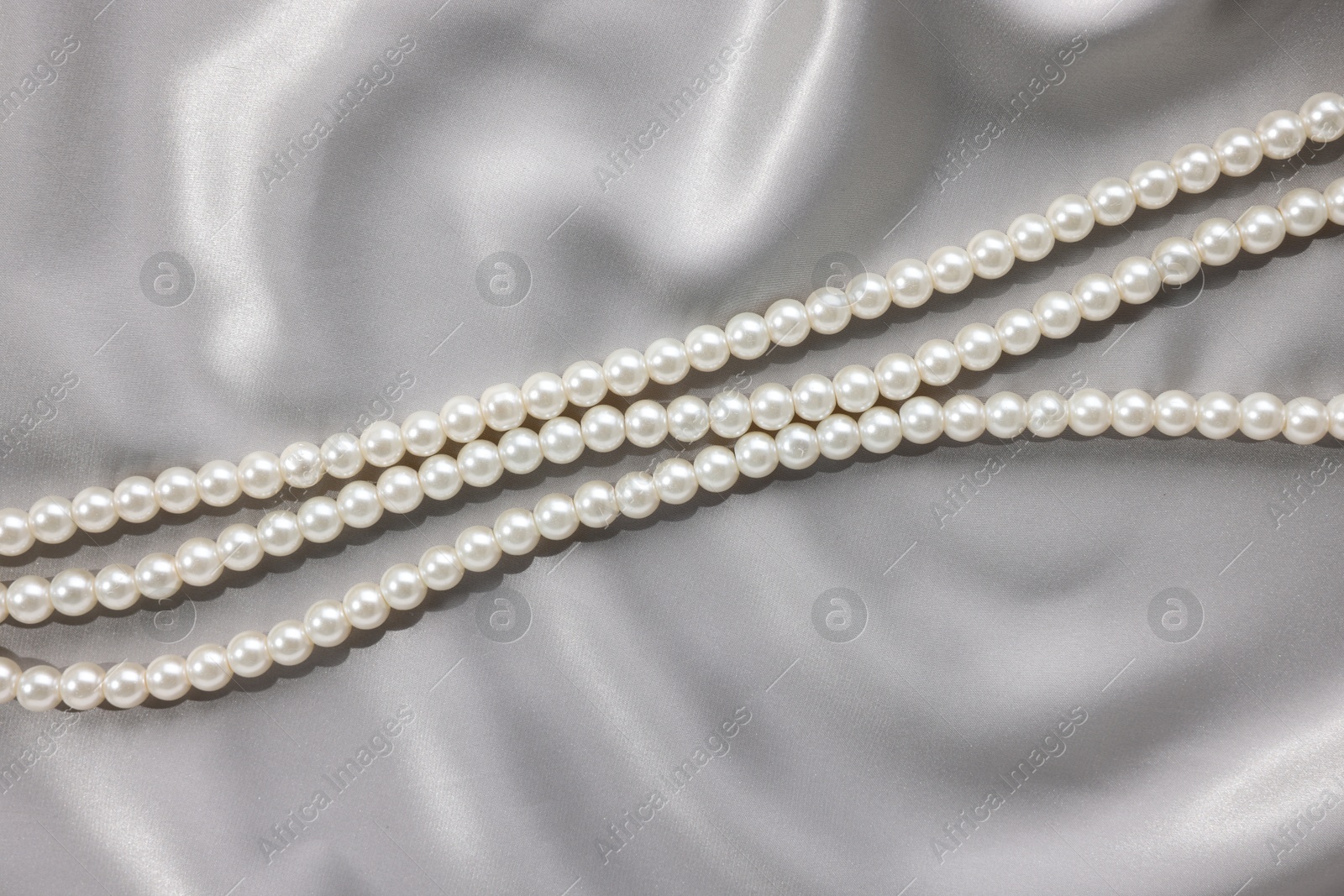 Photo of Beautiful pearl necklace on grey silk, top view