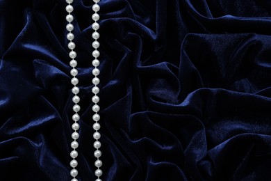 Photo of Beautiful pearl necklace on blue cloth, top view. Space for text