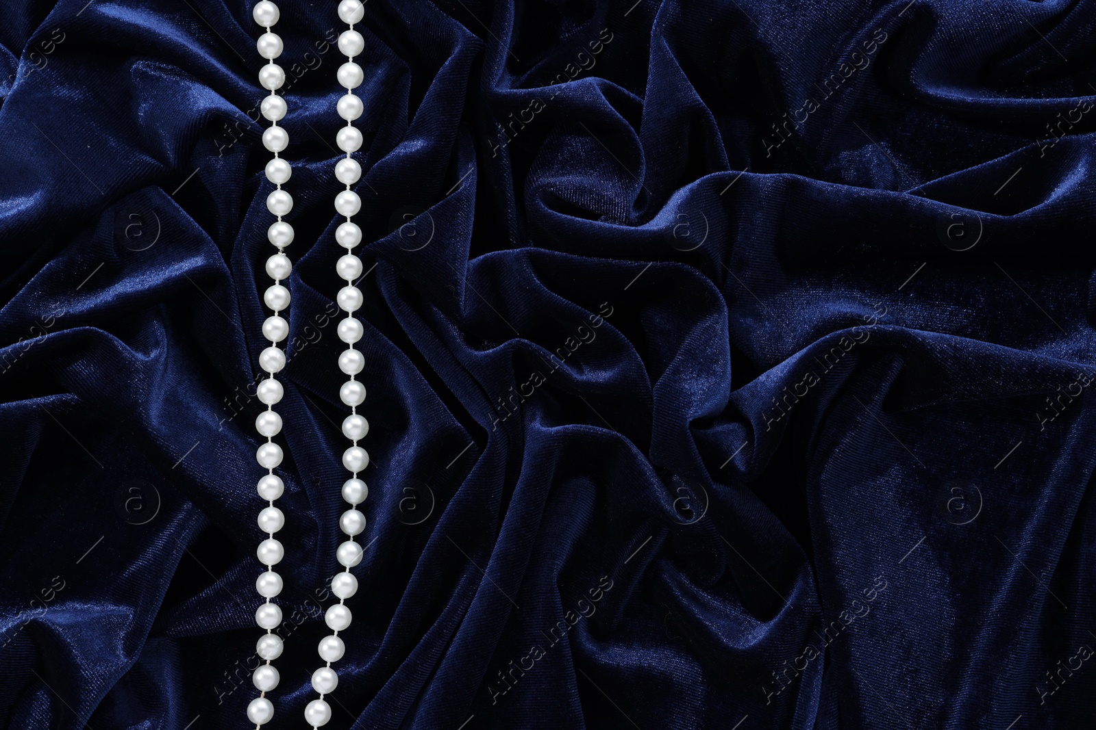 Photo of Beautiful pearl necklace on blue cloth, top view. Space for text