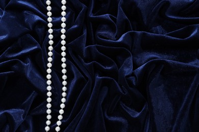 Photo of Beautiful pearl necklace on blue cloth, top view. Space for text