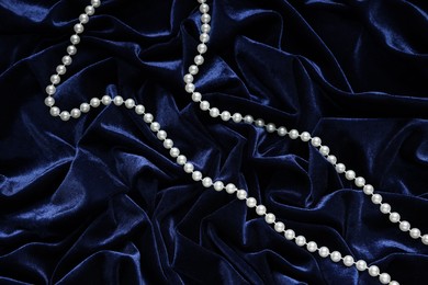 Photo of Beautiful pearl necklace on blue cloth, top view