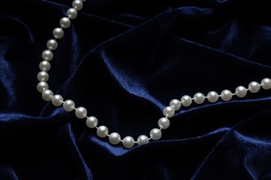 Photo of Beautiful pearl necklace on blue cloth, above view