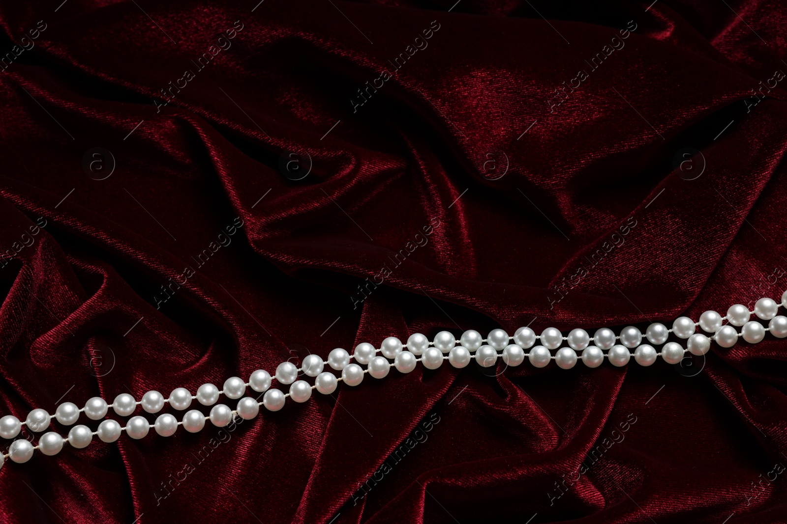 Photo of Beautiful pearl necklace on red cloth, top view. Space for text