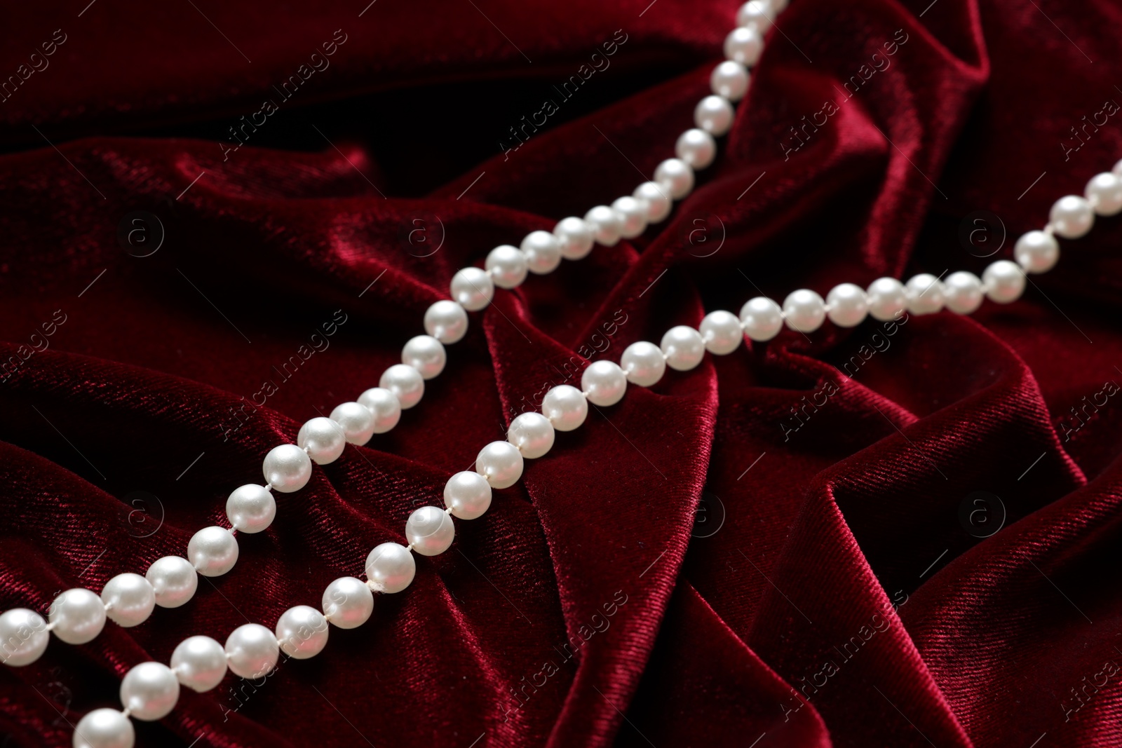 Photo of Beautiful pearl necklace on red cloth, above view