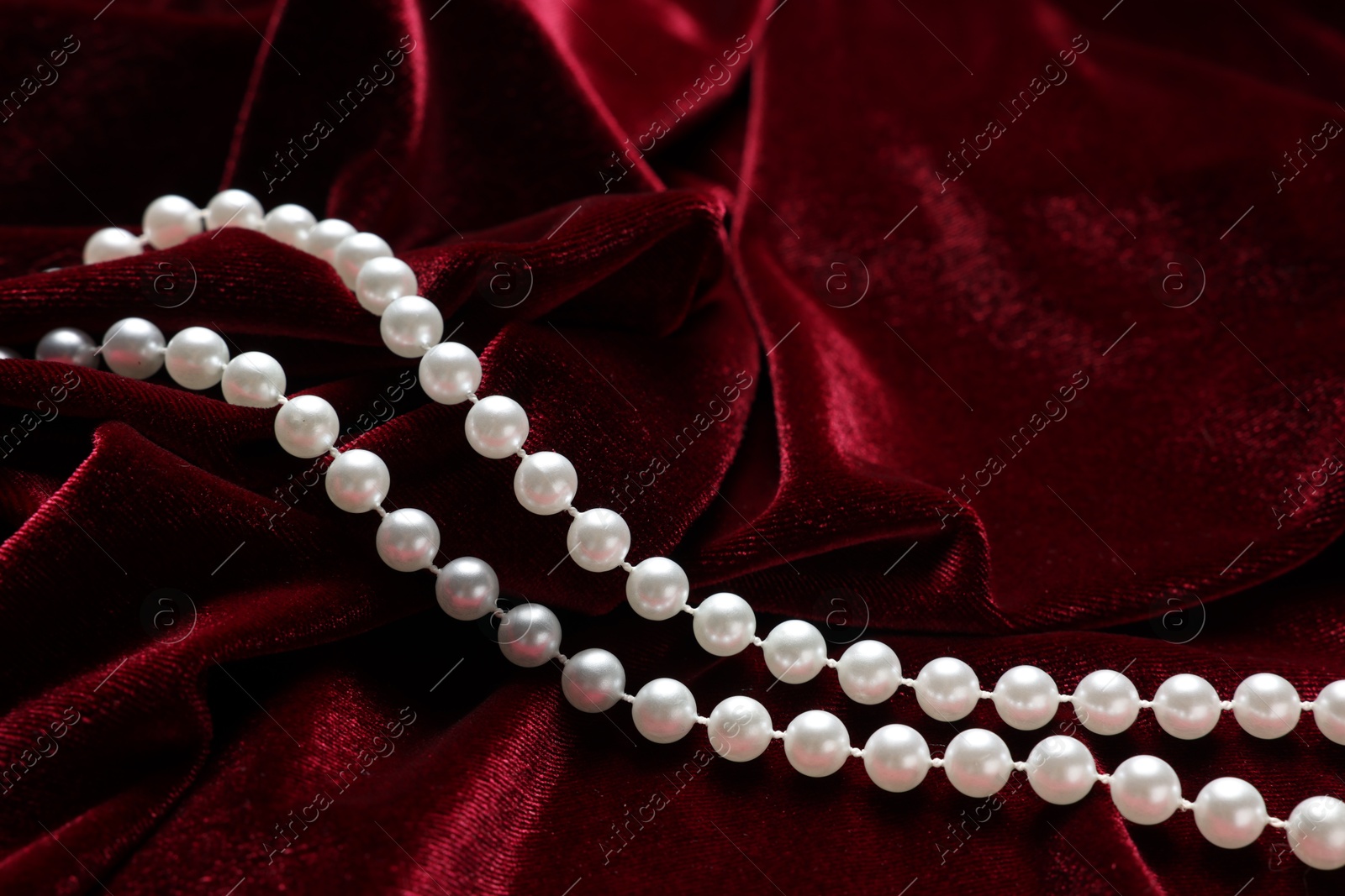 Photo of Beautiful pearl necklace on red cloth, closeup