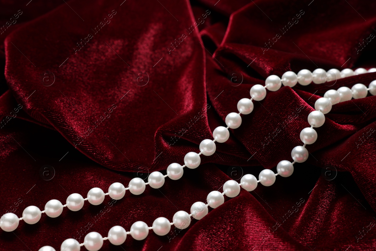 Photo of Beautiful pearl necklace on red cloth, above view