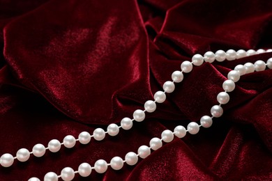 Photo of Beautiful pearl necklace on red cloth, above view