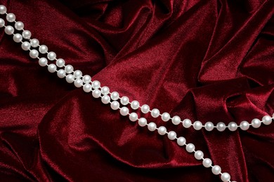 Photo of Beautiful pearl necklace on red cloth, top view