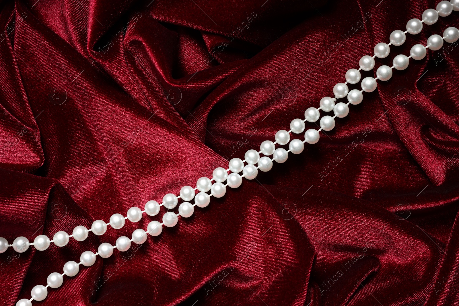 Photo of Beautiful pearl necklace on red cloth, top view