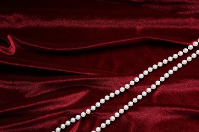 Photo of Beautiful pearl necklace on red cloth, top view. Space for text