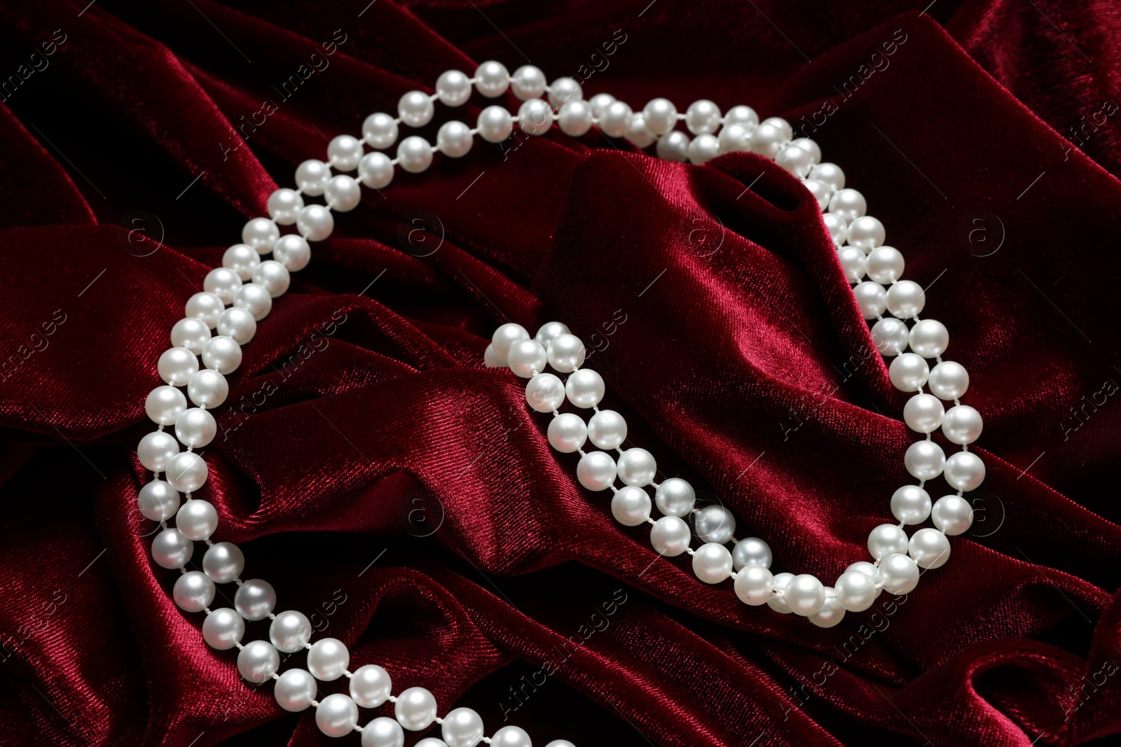 Photo of Beautiful pearl necklace on red cloth, above view