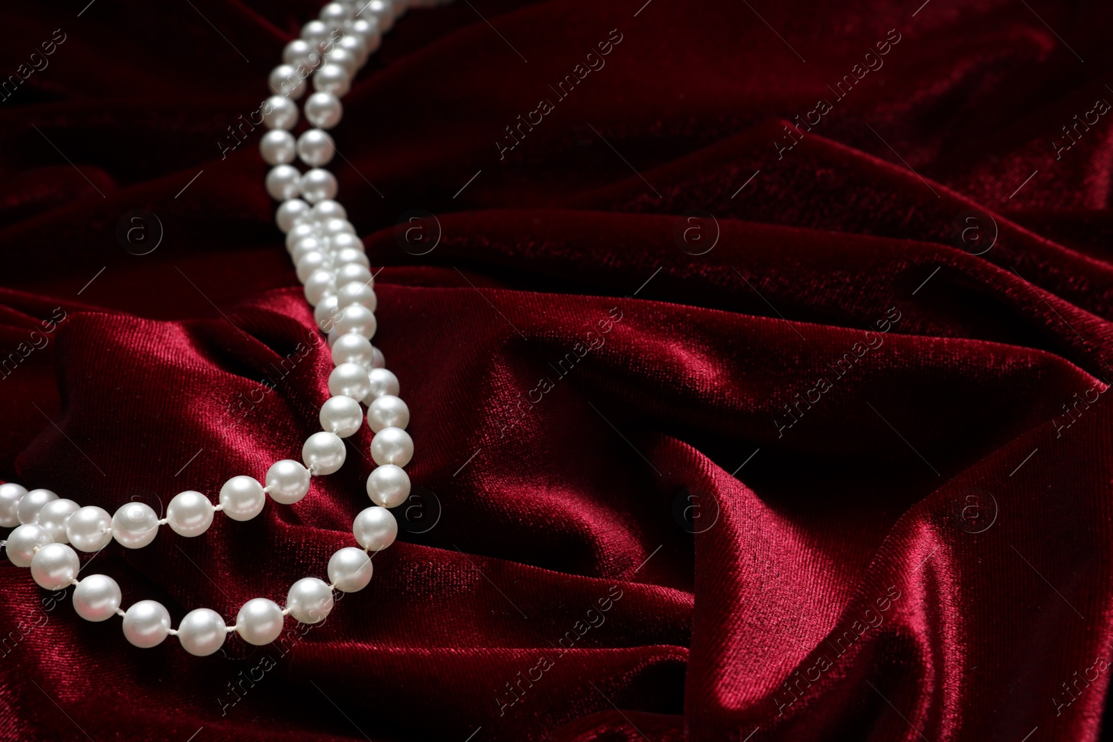 Photo of Beautiful pearl necklace on red cloth, closeup. Space for text