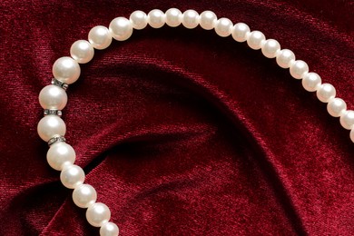 Photo of Beautiful pearl necklace on red cloth, top view