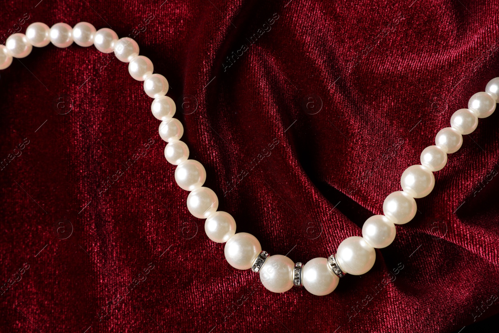 Photo of Beautiful pearl necklace on red cloth, top view