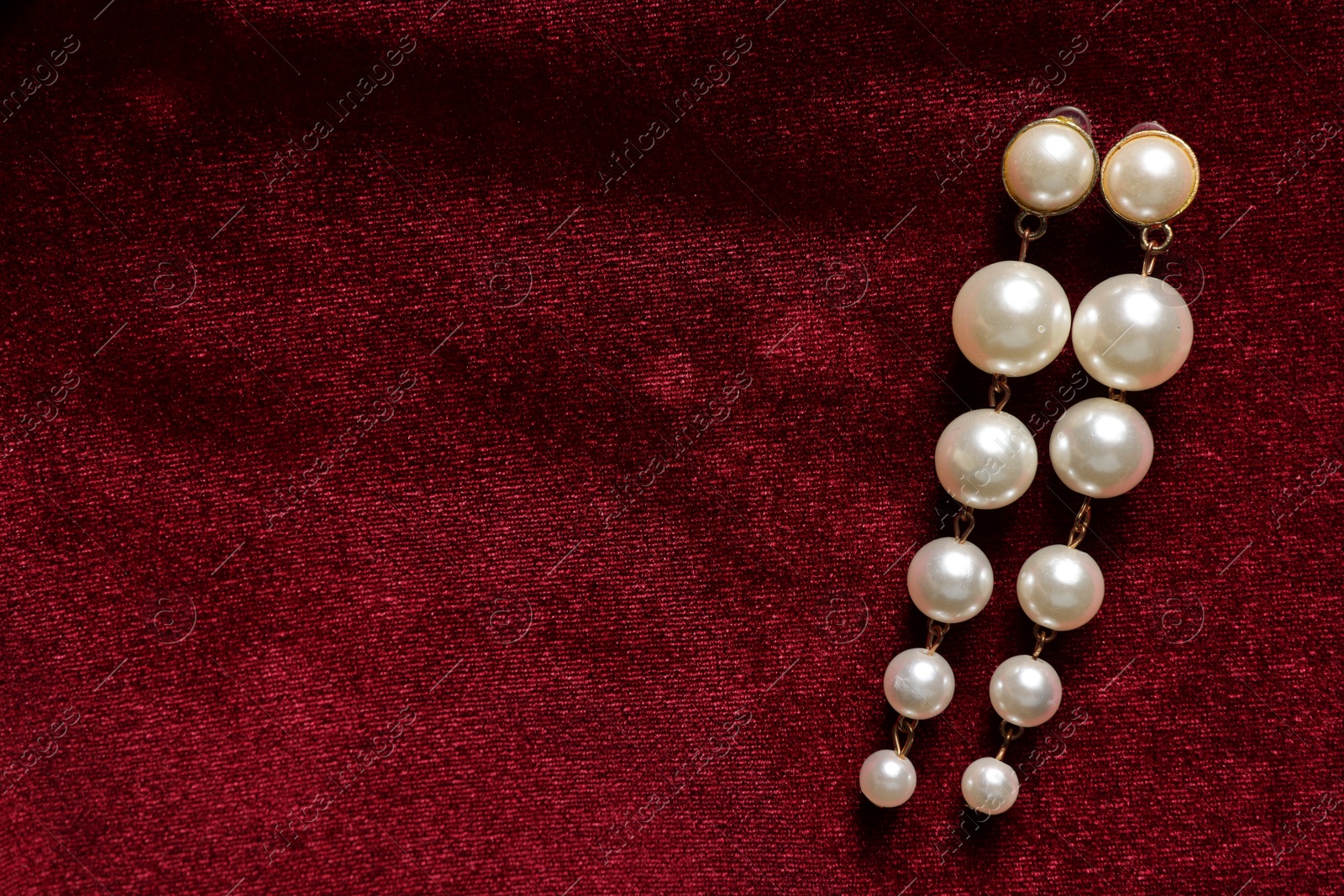 Photo of Beautiful pearl earrings on red cloth, top view. Space for text