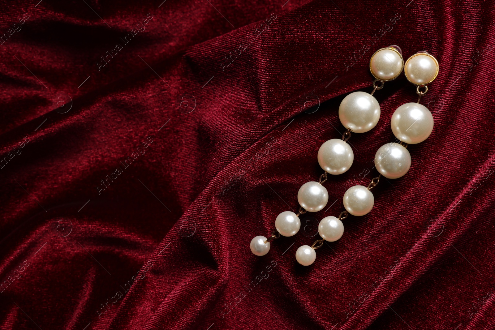 Photo of Beautiful pearl earrings on red cloth, top view. Space for text