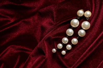 Photo of Beautiful pearl earrings on red cloth, top view. Space for text