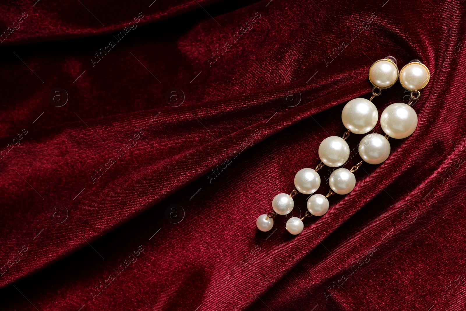 Photo of Beautiful pearl earrings on red cloth, top view. Space for text