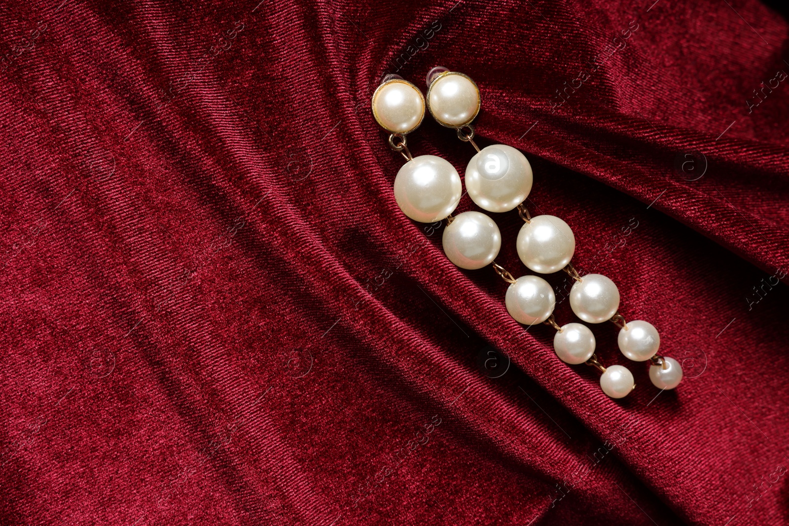 Photo of Beautiful pearl earrings on red cloth, top view. Space for text