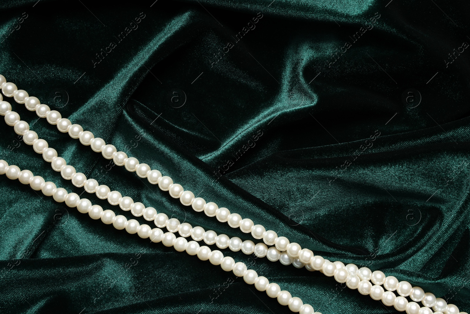 Photo of Beautiful pearl necklace on green cloth, top view. Space for text