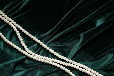 Photo of Beautiful pearl necklace on green cloth, top view. Space for text