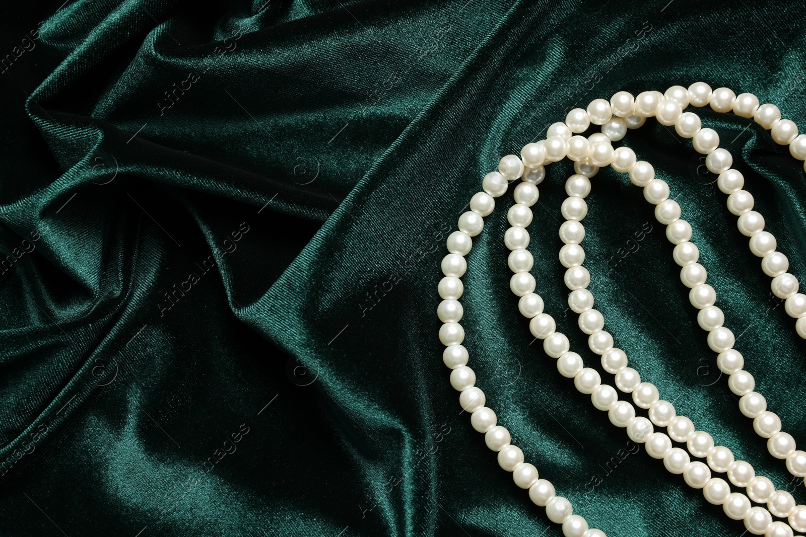 Photo of Beautiful pearl necklace on green cloth, top view. Space for text