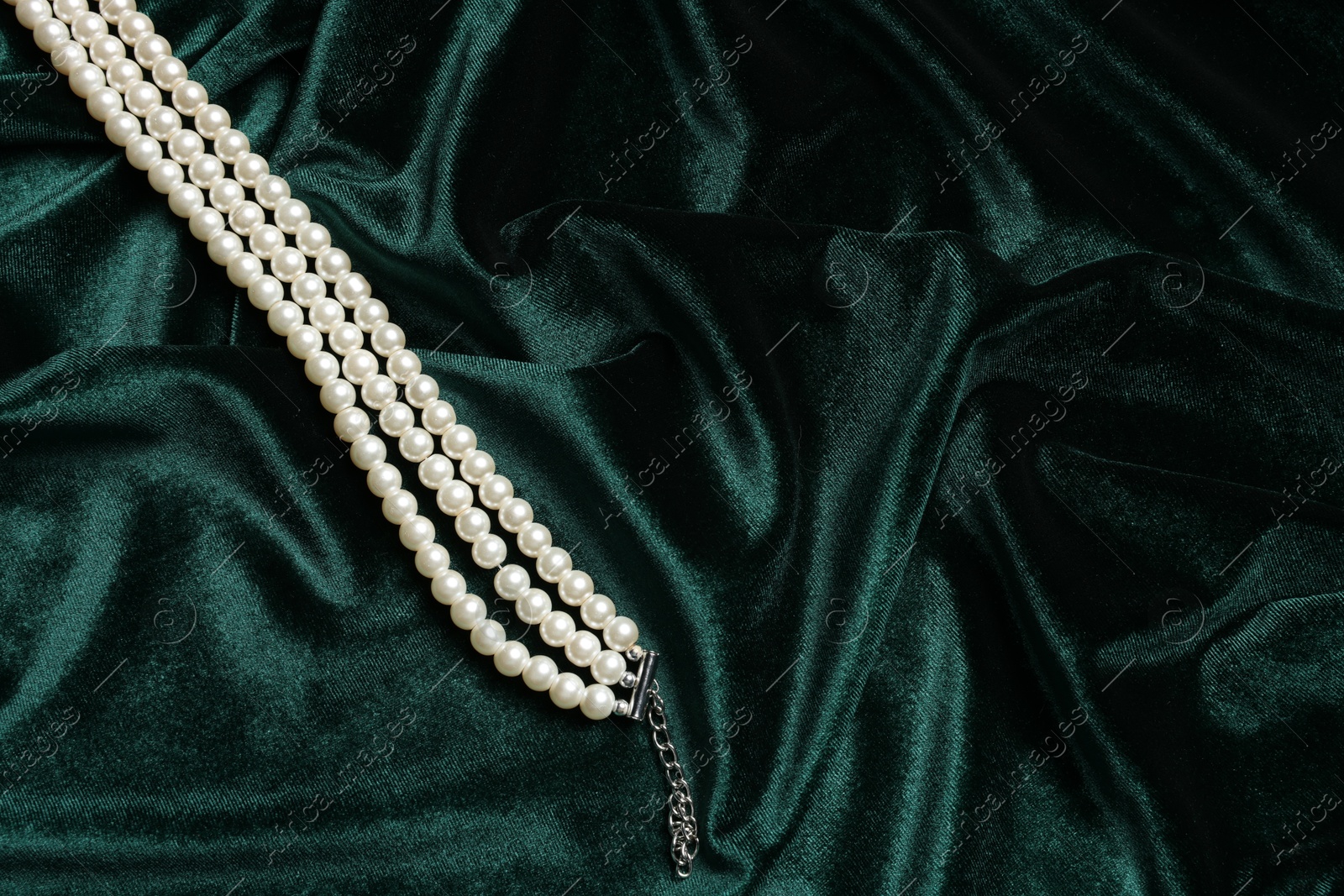 Photo of Beautiful pearl necklace on green cloth, top view. Space for text