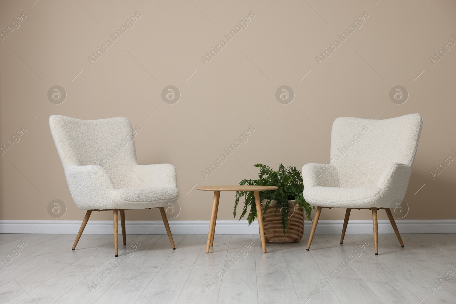 Photo of Soft armchairs and coffee table near beige wall indoors