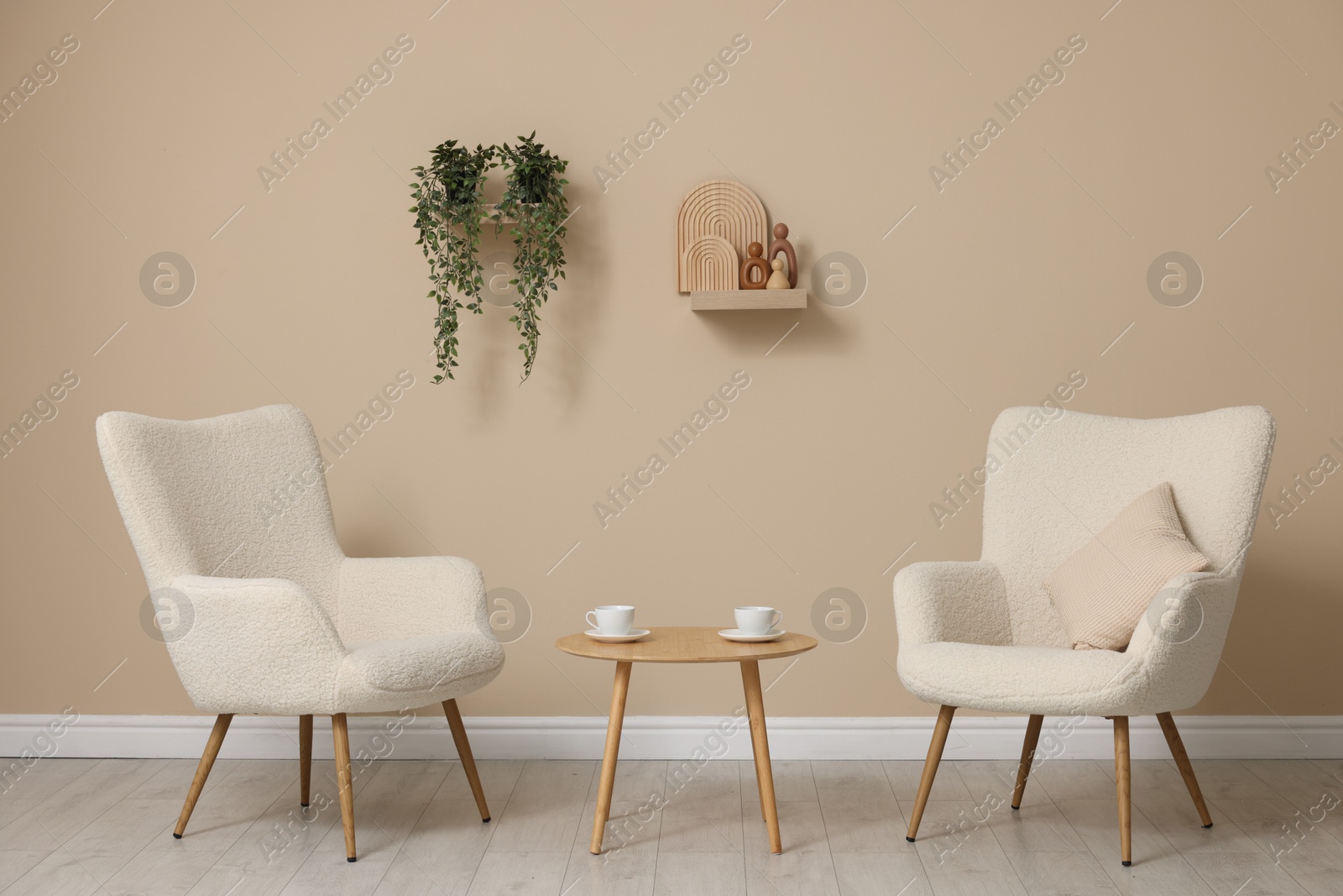 Photo of Soft armchairs and coffee table near beige wall indoors