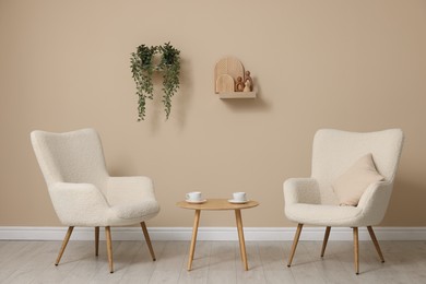 Soft armchairs and coffee table near beige wall indoors