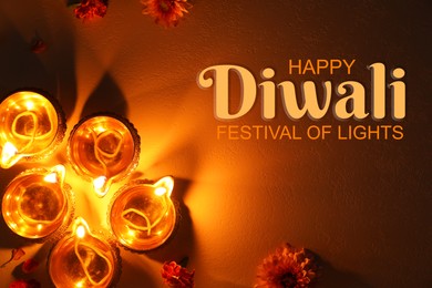 Image of Happy Diwali greeting card, Hindu festival of lights. Diya lamps and beautiful flowers on dark textured surface, flat lay