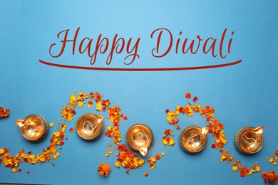 Image of Happy Diwali greeting card, Hindu festival of lights. Diya lamps and marigold petals on light blue background, flat lay