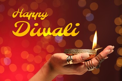 Image of Happy Diwali greeting card, Hindu festival of lights. Woman holding lit diya lamp on red background with blurred lights, closeup