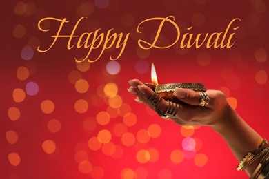 Image of Happy Diwali greeting card, Hindu festival of lights. Woman holding lit diya lamp on red background with blurred lights, closeup